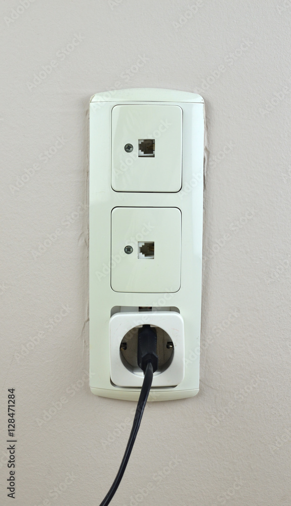Three old used sockets on a wall - two for network cable and one with black electric plug Three old used sockets on a wall - two for network cable and one with black electric plug