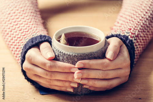 Hot mug of tea warming woman's hands in retro jumper.