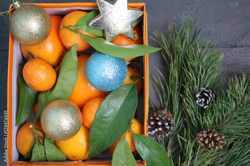 Мандарины и новогодние игрушки в оранжевой коробке и рядом лежит еловая ветка