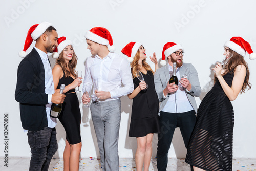 Happy people in santa claus hats drinking champagne and laughing