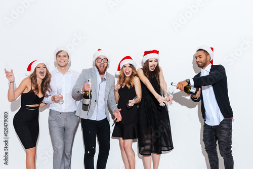 Smiling people in santa claus hats pouring and drinking champagne