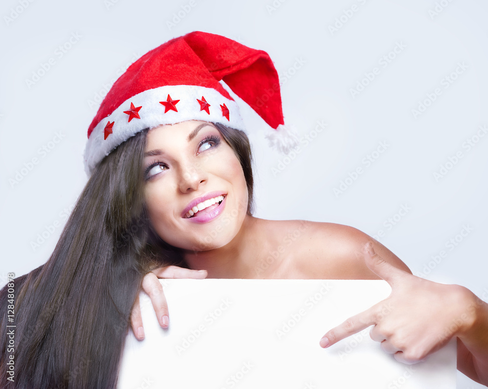 Smiling young woman in Santa hat lean on white banner Smiling young woman in Santa hat lean on white banner