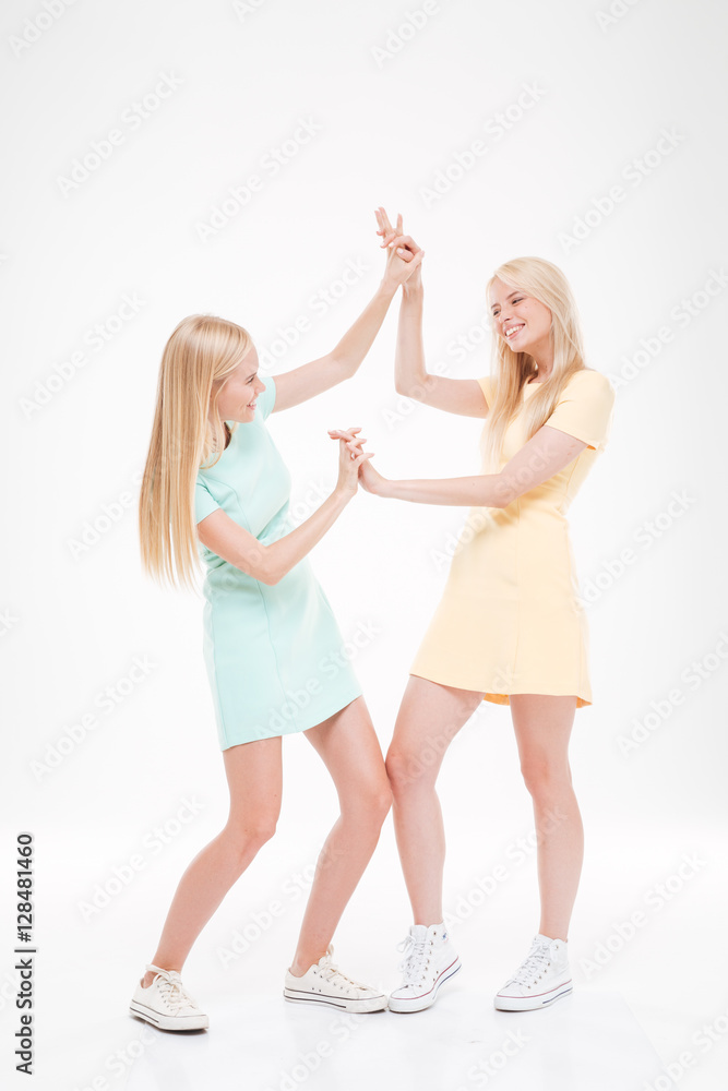 Two playful happy women standing over white background. Two playful happy women standing over white background.