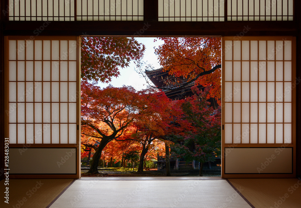 Naklejka premium Ancient pagoda and beautiful red fall maples seen through a traditional Japanese doorway in autumn