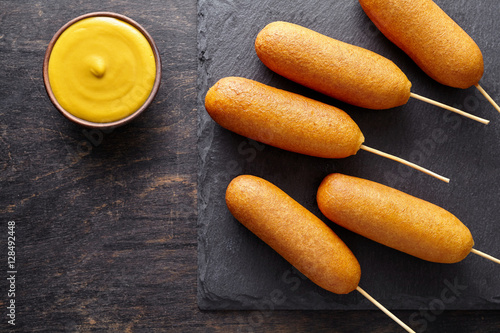 Corn dog traditional American street food deep fried hotdog meat sausage snack treat on stick unhealthy eating on dark wooden background table photo