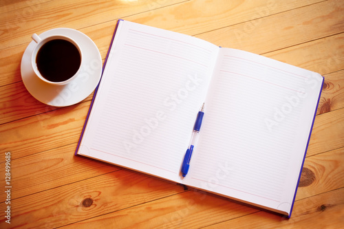 Cup of coffee, pen, opened organizer on the wooden table
