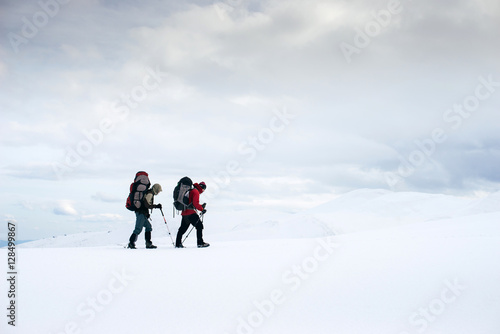 Two friends with backpacks are tracking in the snowy and windy