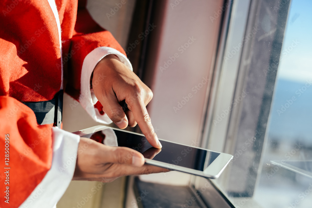 Obraz premium Santa Claus working at desk and using apps on a touch screen tablet