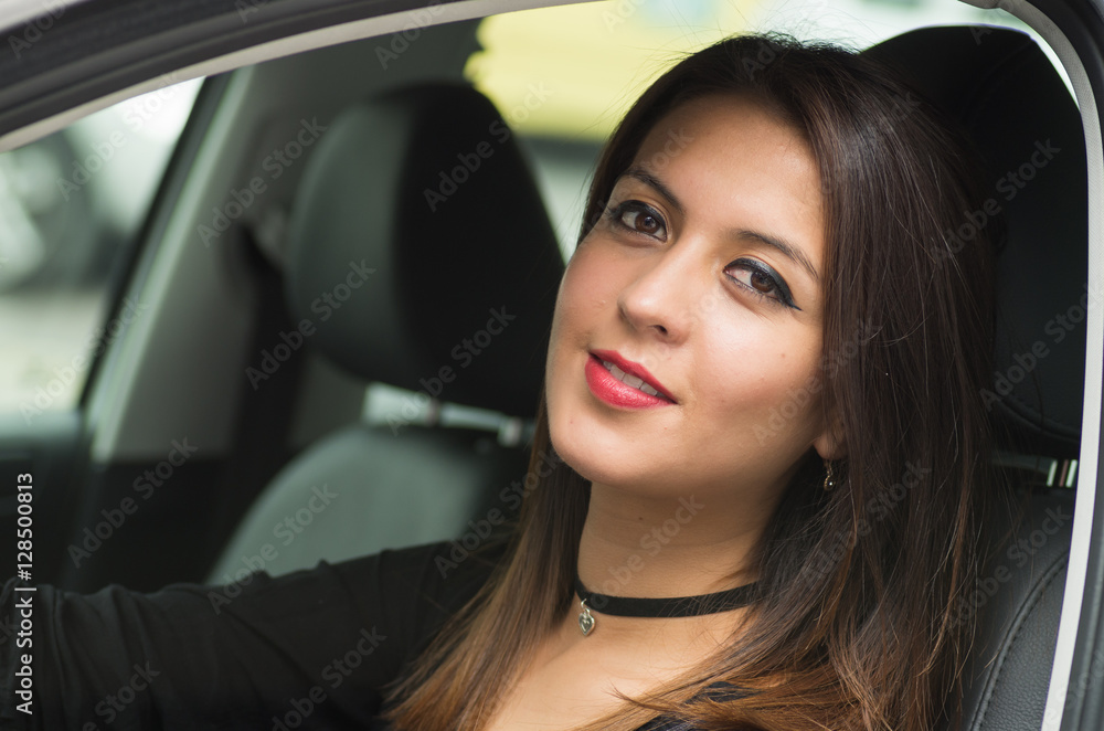 Closeup young woman sitting in car smiling to camera, as seen from outside drivers window, female driver concept