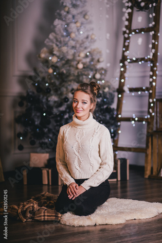 Beautiful young woman posing under Christmas tree in a holiday interior