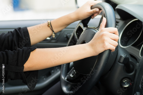 Closeup inside vehicle of hands holding onto steering wheel, black interior background, female driver concept
