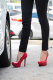Closeup womans legs wearing black jeans and red stilettos standing outside car door, other cars background, female driver concept