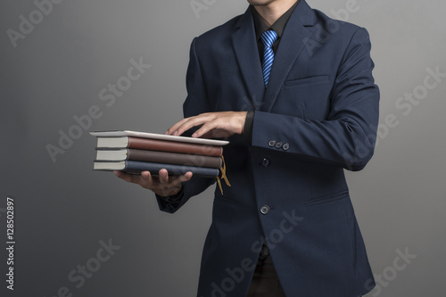 Close up of businessman in blue suit holding books on gray backg