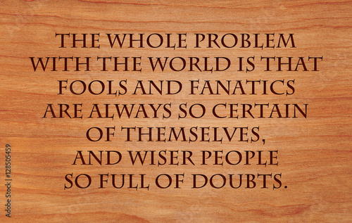 The whole problem with the world is that fools and fanatics are always so certain of themselves, and wiser people so full of doubts - quote on wooden red oak background photo