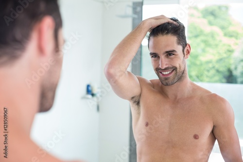 Shirtless young man smiling while looking in mirror 