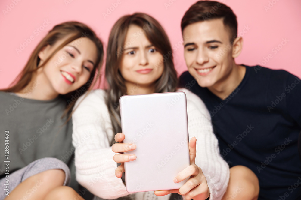 Young beautiful friends making selfie on tablet over pink background. Young beautiful friends making selfie on tablet over pink background.