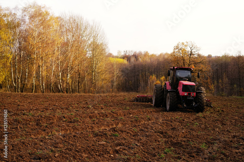 Tractor in the field plows the earth in sunny autumn day