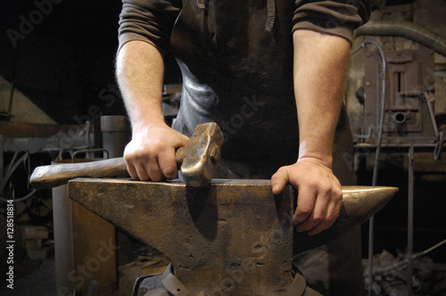 Blacksmith standing and holding hammer in hand on the anvil in forge