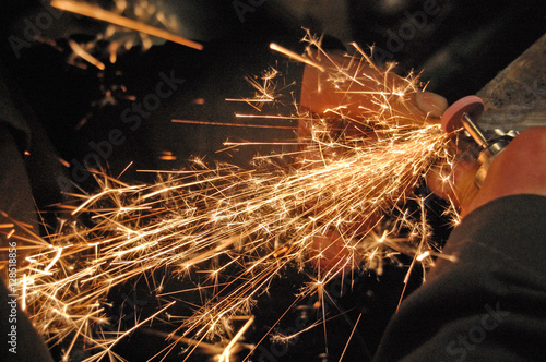 Blacksmith grinding detail at his workshop.  Image full of sparkles
