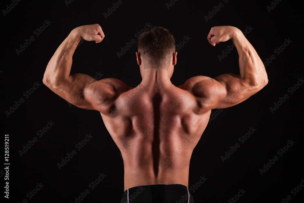 Rear view of healthy muscular young man with his arms stretched out isolated on black background Rear view of healthy muscular young man with his arms stretched out isolated on black background