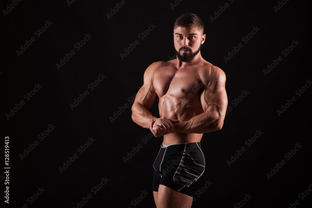 Handsome muscular bodybuilder posing over black background.