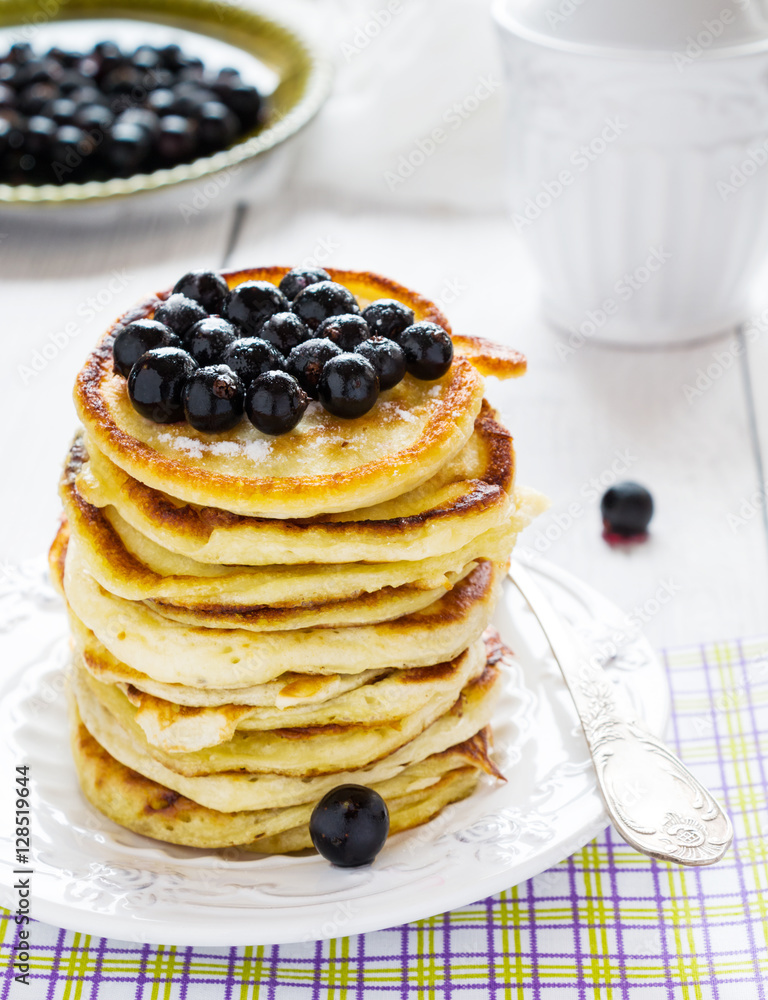 Stack of homemade pancakes with black currant, vintage white plate and fork, wooden table.