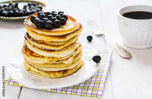 Stack of homemade pancakes with black currant, vintage white plate and fork, cup of coffee, wooden table.