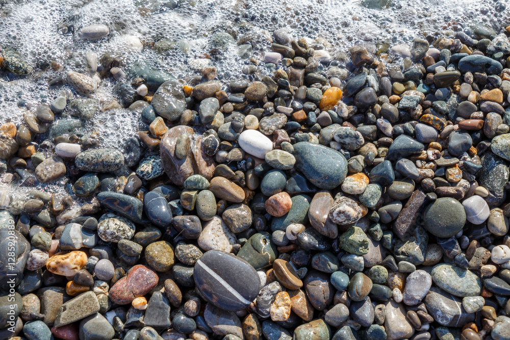 Wet bright shining different colored pebble stones and sea foam Wet bright shining different colored pebble stones and sea foam