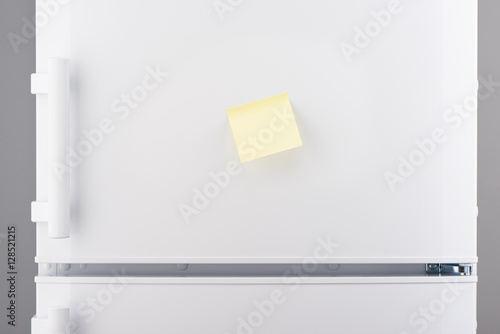 Blank light yellow sticky paper note on white refrigerator