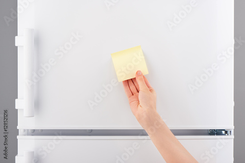 Hand holding yellow sticky paper note on white refrigerator