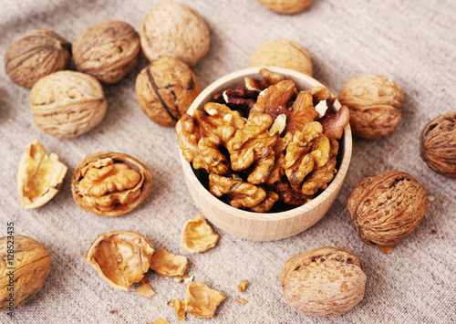 Walnut kernels in a wooden bowl and whole walnuts on table. Walnuts