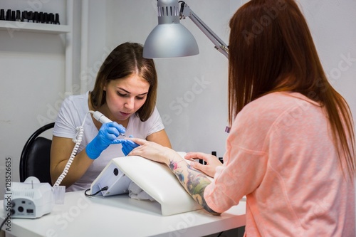 Hardware manicure in a beauty salon. Manicurist is applying electric nail file drill to manicure on female fingers.