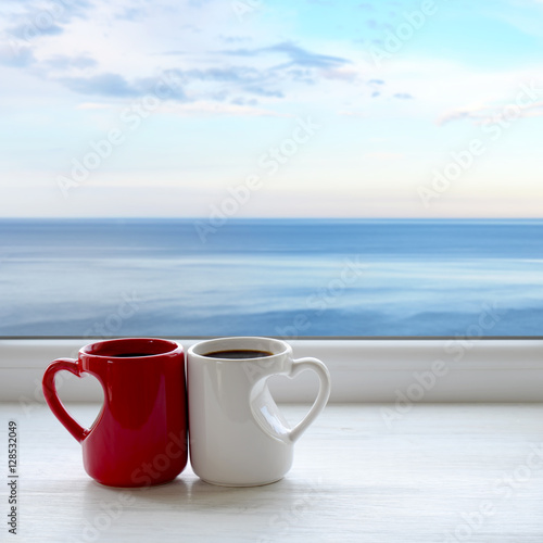 Two cups of coffee on a windowsill. In the background sea and sky