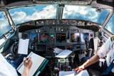 Airplane cockpit flying in a cloudy blue sky at day. with pilots arms and blank white papers for copy space.