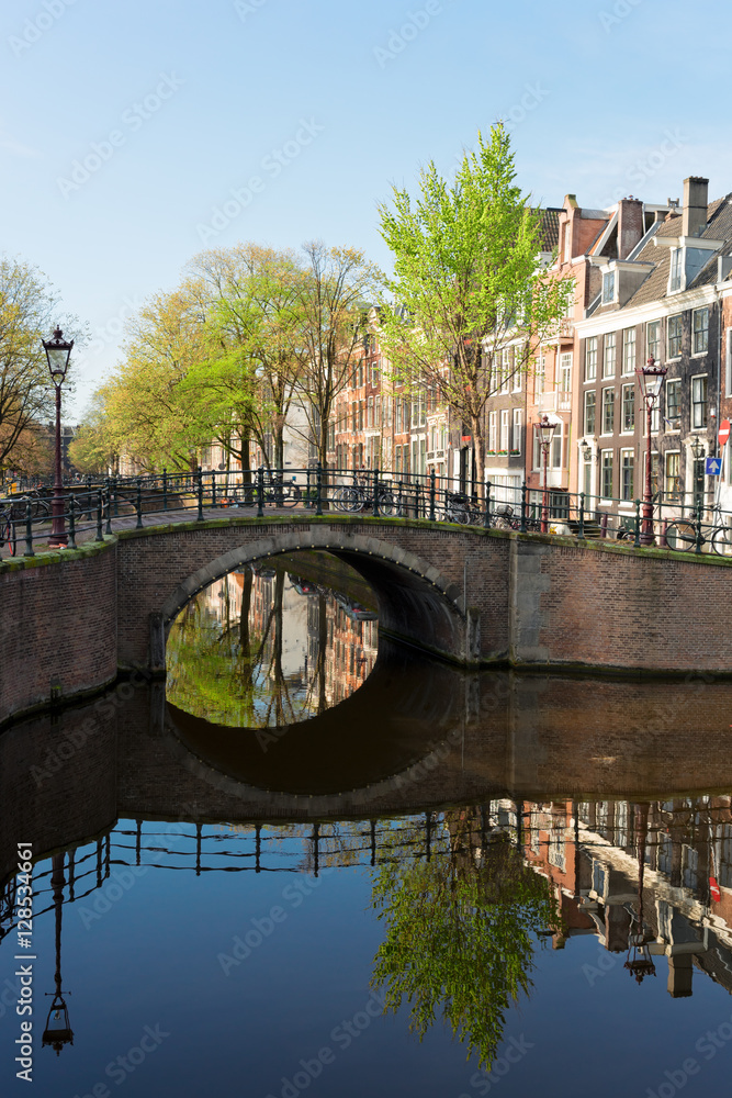 Fototapeta premium Historical bridge over canal with mirror reflections in water, Amstardam, Netherlands