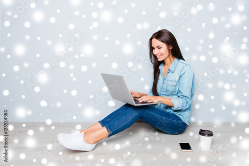 Young smiling woman working on laptop while sitting on floor on