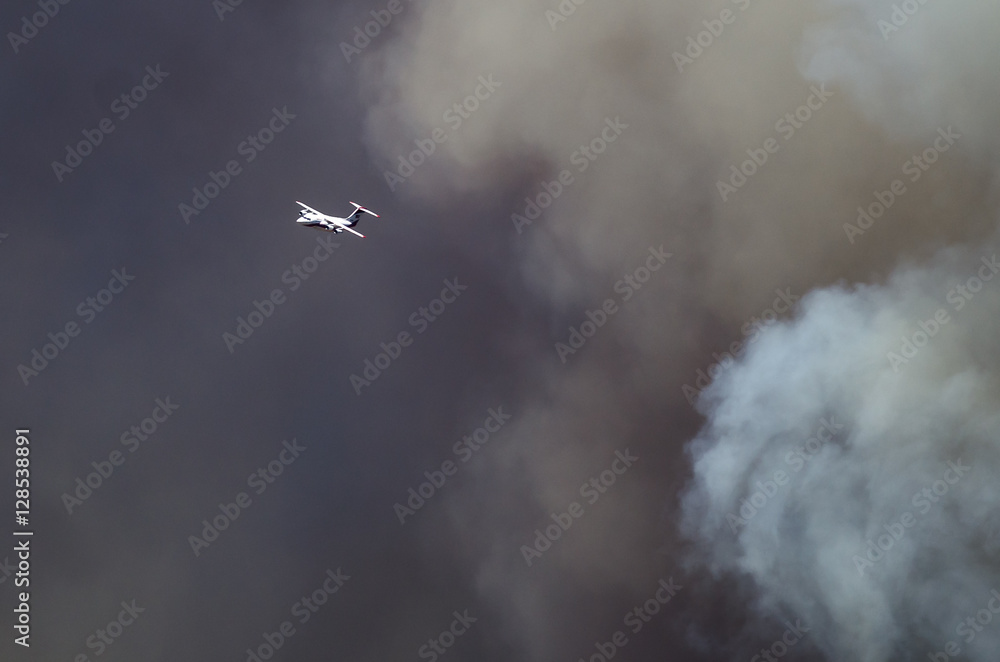 White Aircraft Flying Ahead of the Dense White Smoke Rising from the Raging Wildfire White Aircraft Flying Ahead of the Dense White Smoke Rising from the Raging Wildfire