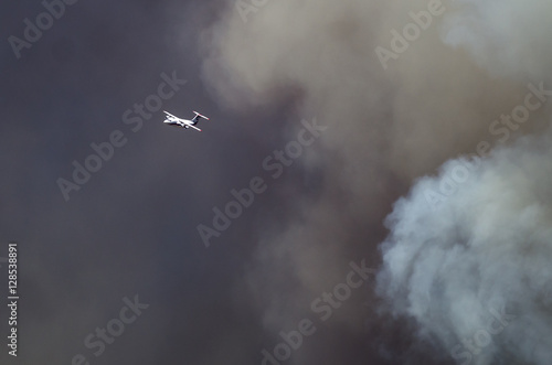 White Aircraft Flying Ahead of the Dense White Smoke Rising from the Raging Wildfire
