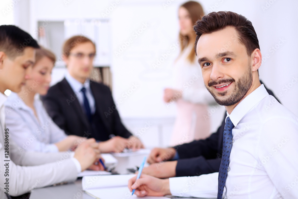 Portrait of cheerful smiling businessman against a group of people at meeting. Portrait of cheerful smiling businessman against a group of people at meeting.