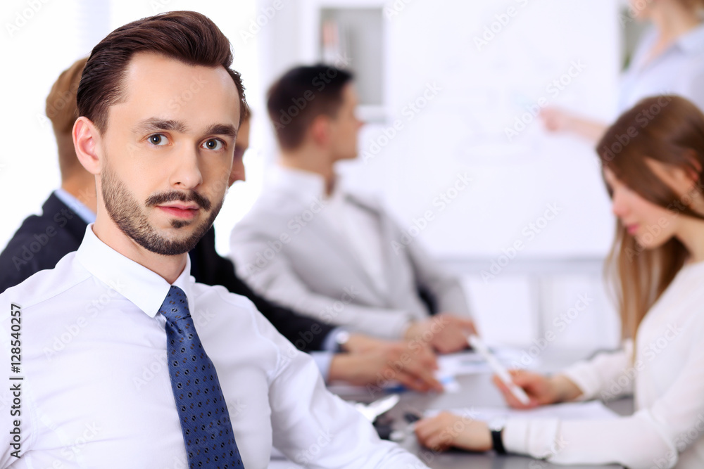 Portrait of cheerful smiling businessman against a group of people at meeting. Portrait of cheerful smiling businessman against a group of people at meeting.