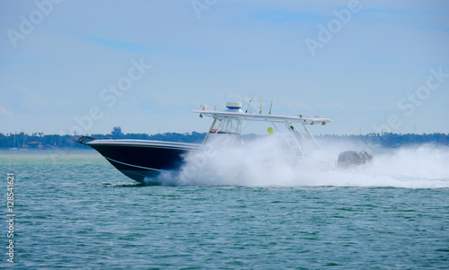 High speed scuba diving sport fishing boat with three motors is cruising very fast with big water spray coming off of bow and hull