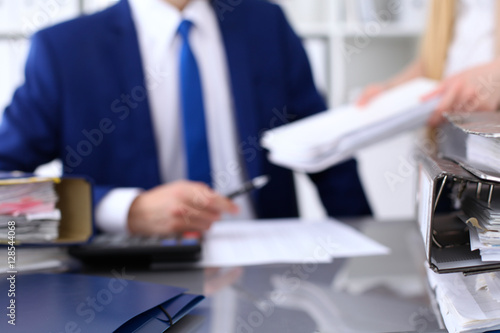 Binders with papers are waiting to be processed with businessman and secretary back in blur. Accounting planning budget, audit, insurance  and business concept © rogerphoto