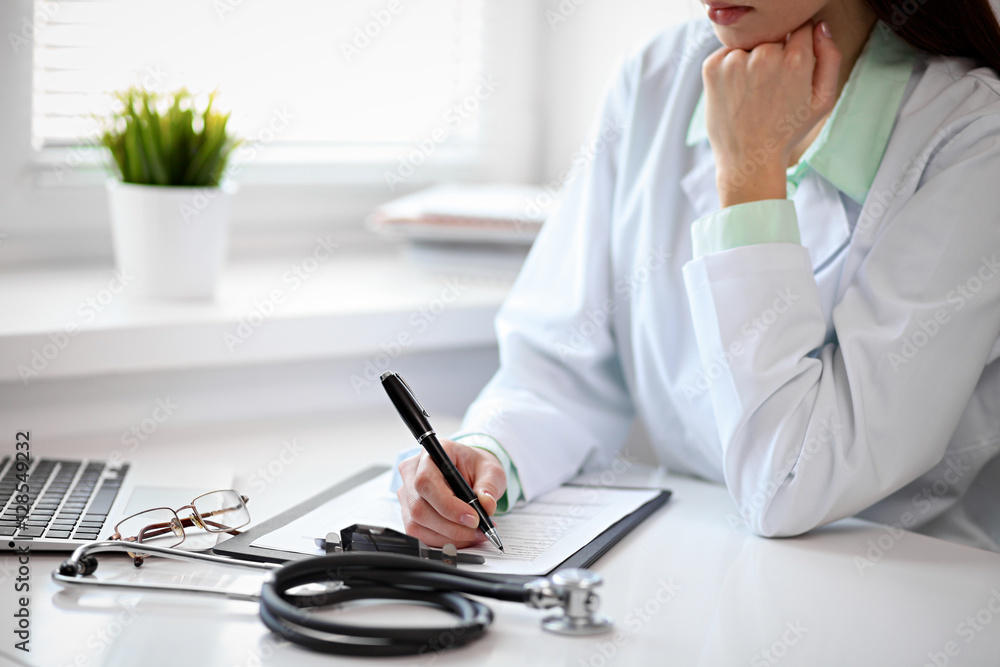 Close up of unknown female doctor sitting at the table near the window in hospital and typing at laptop computer Close up of unknown female doctor sitting at the table near the window in hospital and typing at laptop computer