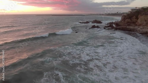 moving aerial imagery above breaking waves and rocks during a on a windy day during a colorful sunset in the Corona Del Mar Neighborhood of Newport Beach, California,