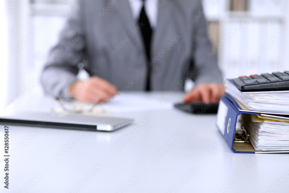 Fototapeta premium Binders with papers are waiting to be processed with business woman back in blur. Accounting planning budget, audit and insurance concept