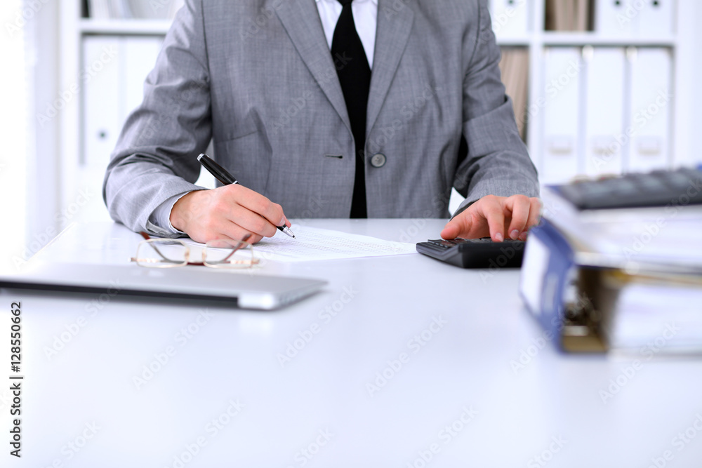Bookkeeper or female financial inspector making report, calculating or checking balance. Internal Revenue Service checking financial document. Audit concept. Bookkeeper or female financial inspector making report, calculating or checking balance. Internal Revenue Service checking financial document. Audit concept.