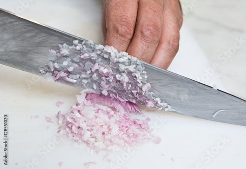 A knife dicing fresh organic Shallots, on a white cutting board.