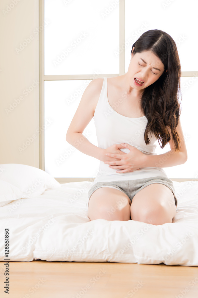 Beautiful asian woman suffering from stomach pain on bed Beautiful asian woman suffering from stomach pain on bed