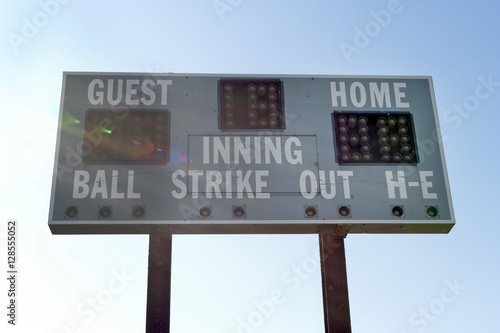 Rural, weathered baseball scoreboard against sky with lens flare. Horizontal.