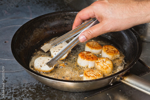 Fotografía Delicious pan seared organic scallops being flipped over and seared in a metal cooking pan on the hob